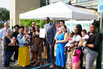 Mothers with their babies, Dr. Mona Hanna, Lt. Governor Gilchrist standing outside under a tent celebrating. 