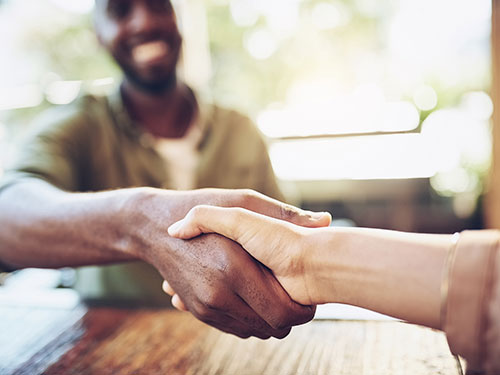 A close-up of two hands shaking in a friendly manner, with a blurred background suggesting a casual setting