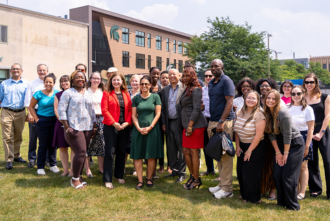 Group photo of Flint Registry team with speakers from the press event standing in front of the MSU Flint building